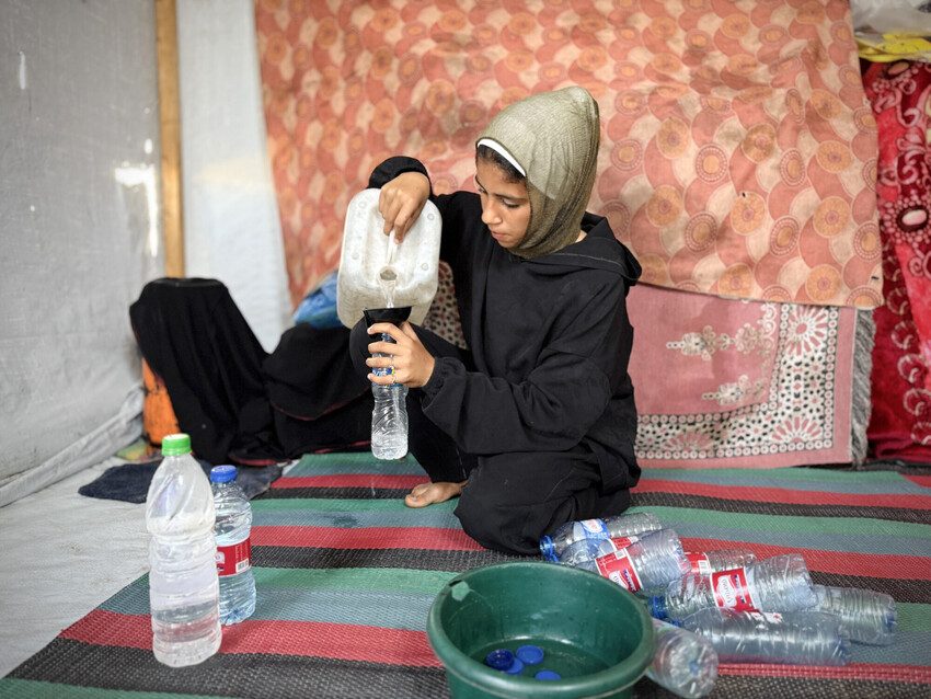 A teenage girl fills plastic bottles with water in Gaza.