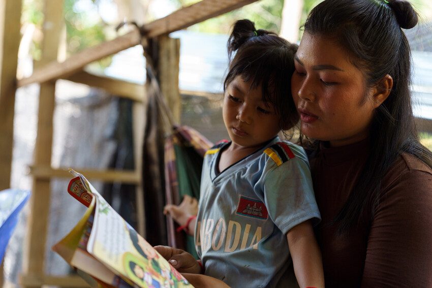 Kanada is reading a book to her daughter who is sitting on her lap.