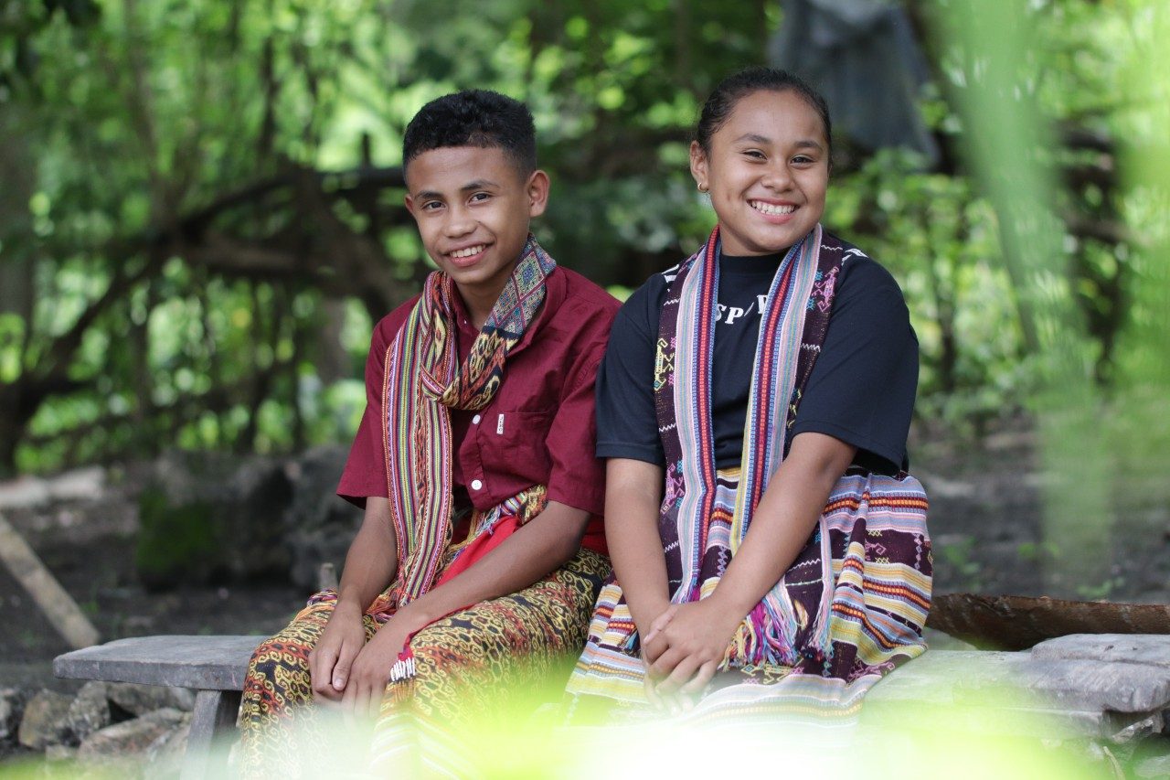 A boy and a girl sitting on a bench,